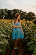 Woman in a fitted blue mini dress standing in a green grass field — placeholder image